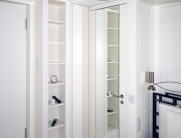 Möbelgestaltung im Schlafzimmer – hohe weiße Regale und Schranktüren mit Spiegeln für ein modernes und elegantes Ambiente.